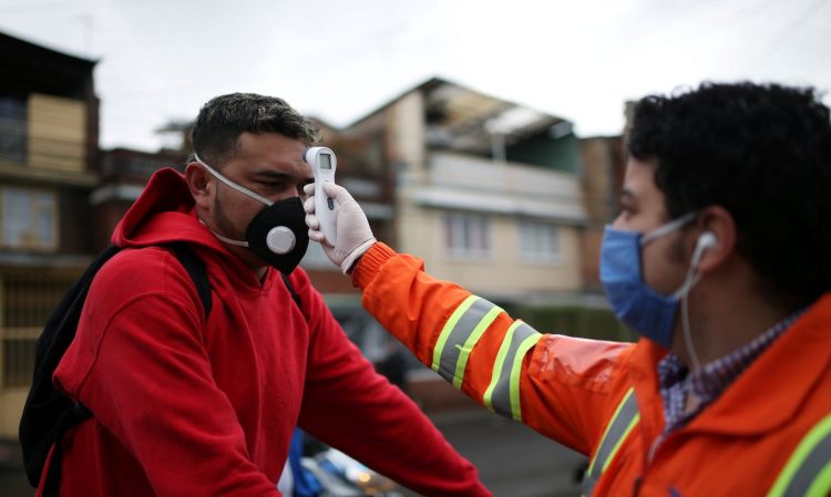 Um funcionário da empresa de construção Amarilo, usando uma máscara facial, mede a temperatura corporal de outro funcionário, em meio ao surto de doença por coronavírus (COVID-19) em Bogotá