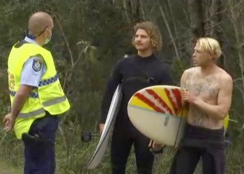 Policial conversa com surfistas na praia de Coffs Harbour, na Austrália — Foto: Australian Broadcasting Corporation/Via AP