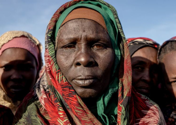 Mulheres e crianças sudanesas deslocadas fazem fila para receber alimentos em um local de distribuição de uma cozinha comunitária da Save the Children no acampamento Daba Naira, em Tawila. Foto: © Unocha/Giles Clarke