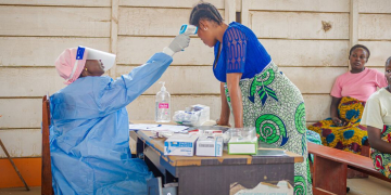 Um profissional de saúde com equipamento de proteção individual verifica a temperatura de uma mulher grávida no leste da República Democrática do Congo, enquanto o surto de Ebola continua. Foto: © Unfpa/Junior Mayindu